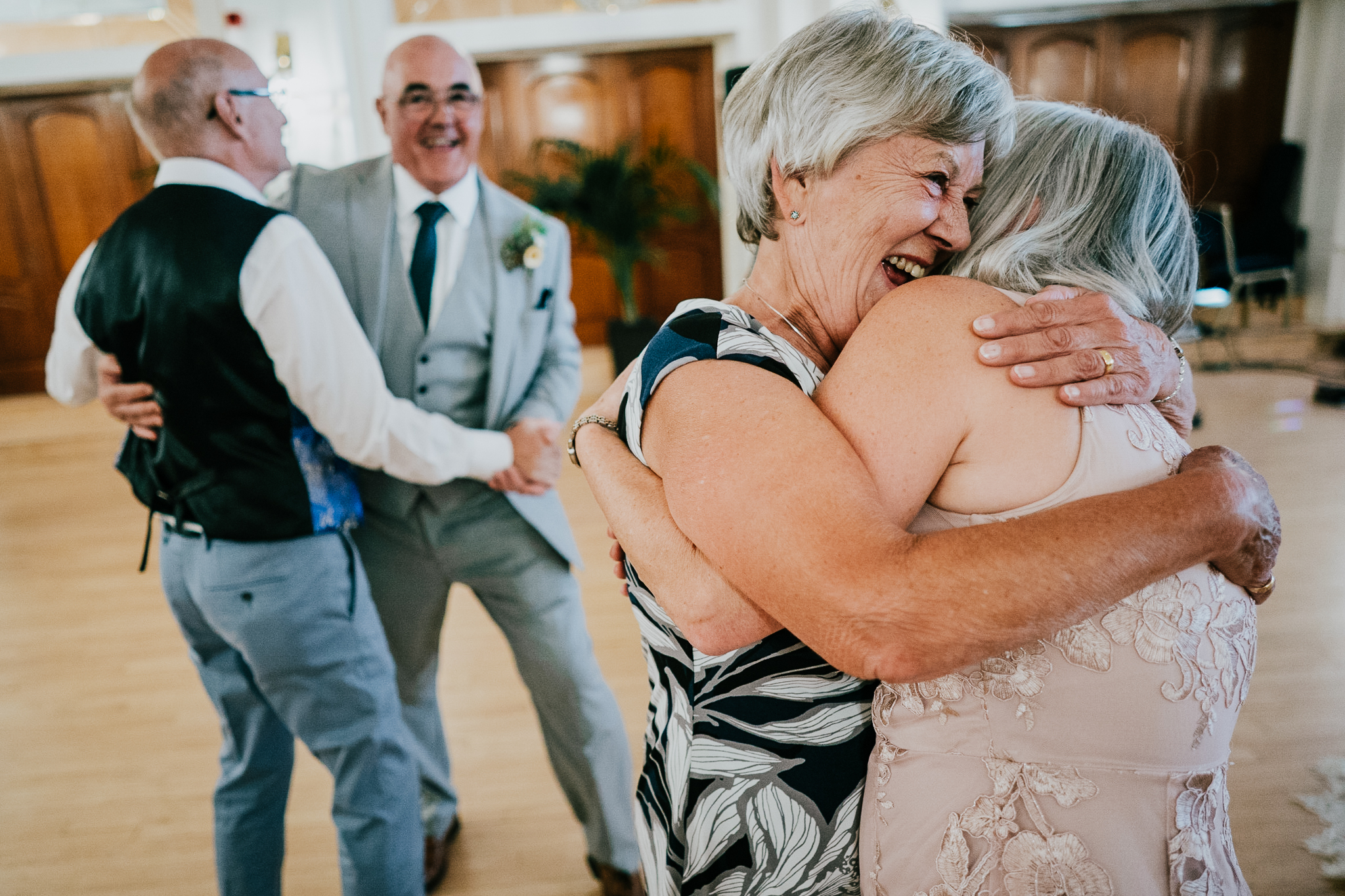 Two wedding guests embrace at The Atlantic Hotel, whilst two other guests dance behind them.