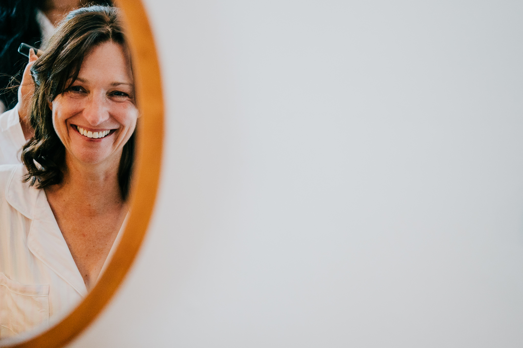 Bride laughing in the mirror, as she gets ready for her wedding at The Horn of Plenty in Devon.