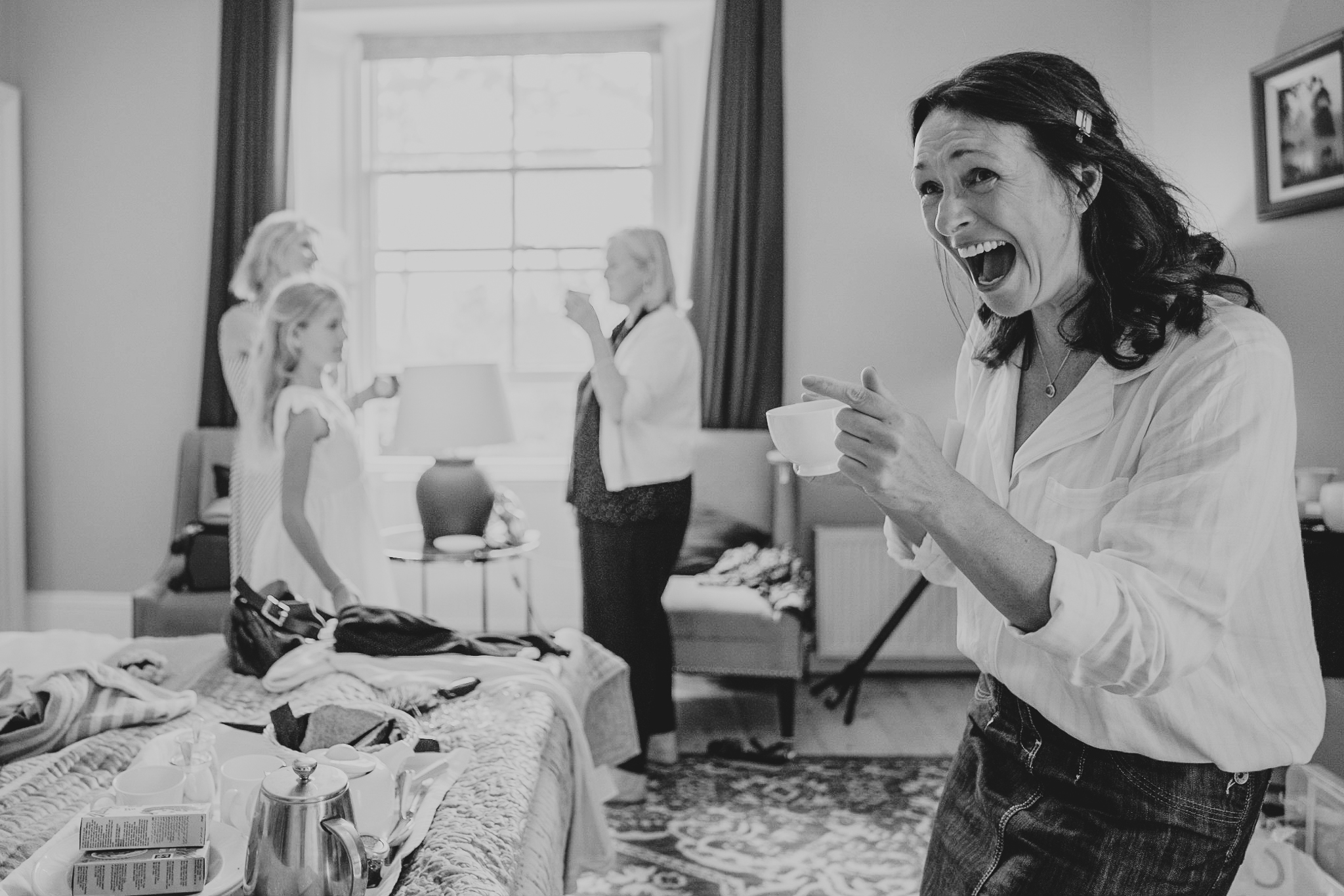 Bride, holding a cup of tea, laughs loudly during wedding prep at The Horn of Plenty.