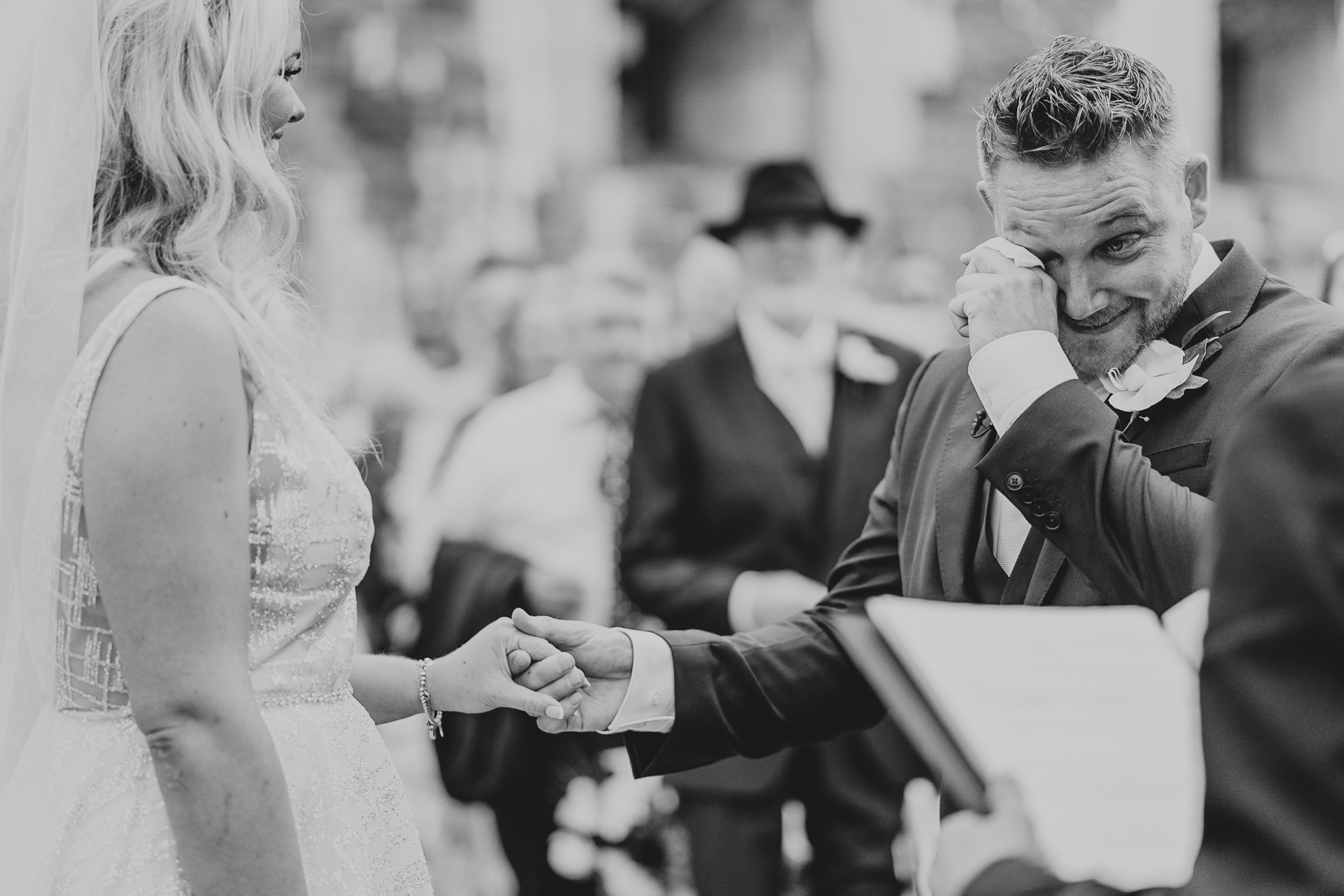 An emotional groom wipes away a tear whilst holding his bride's hand, during their outdoor ceremony at Polhawn Fort.