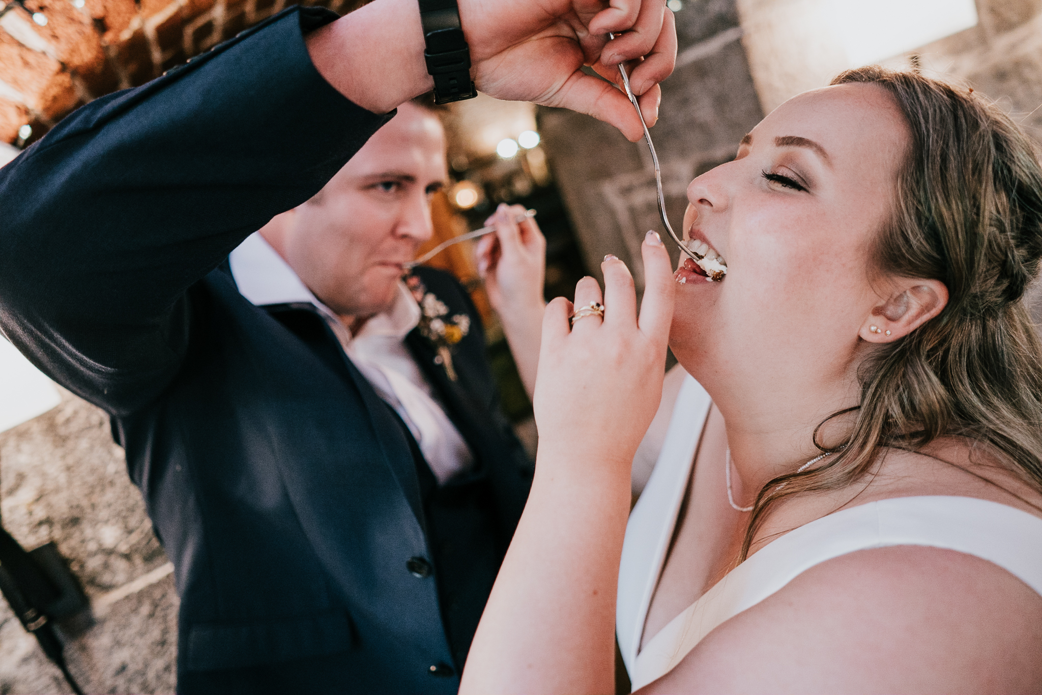 polhawn-fort-wedding-zarra-chris 7 – Alan Law Photography Bride and groom exchanging wedding cake, feeding it into each other's mouths.