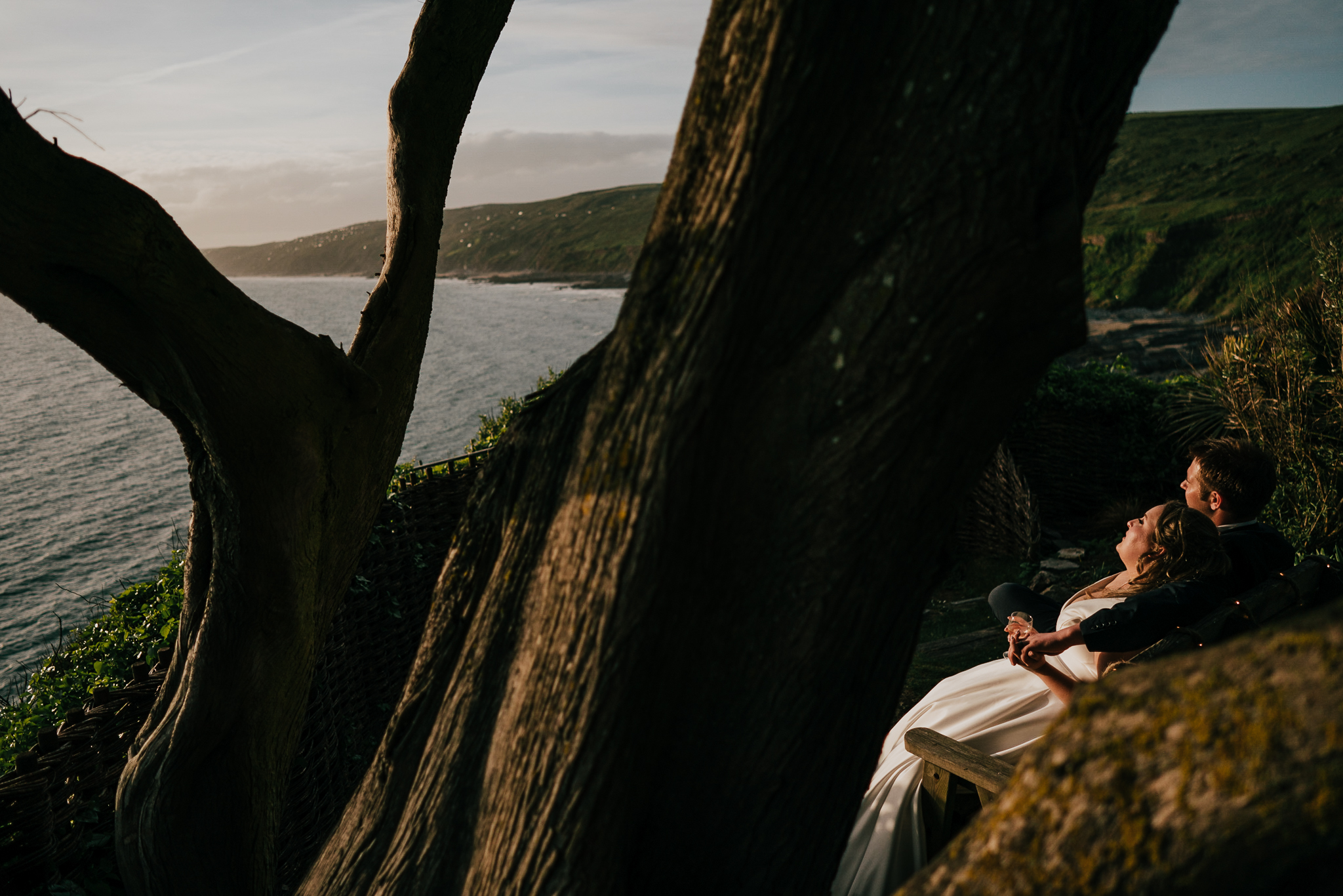 polhawn-fort-wedding-zarra-chris 9 – Alan Law Photography Bride and groom sitting on a bench, enjoying the sunset over the ocean, at Polhawn Fort.