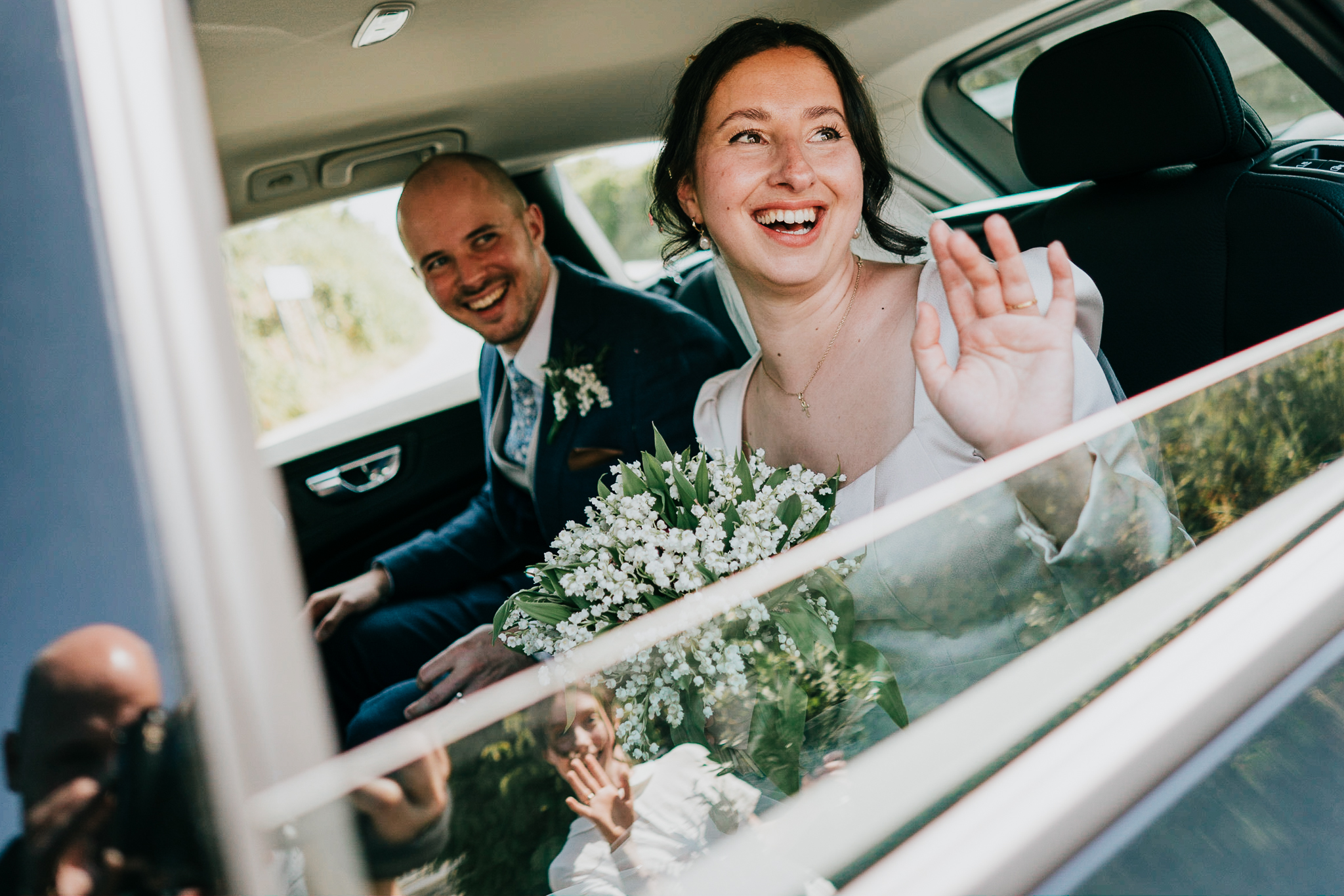 port-isaac-wedding-photographer 1 – Alan Law Photography The bride and groom waving goodbye through the window of their wedding car, at St Endellion Church, Cornwall.